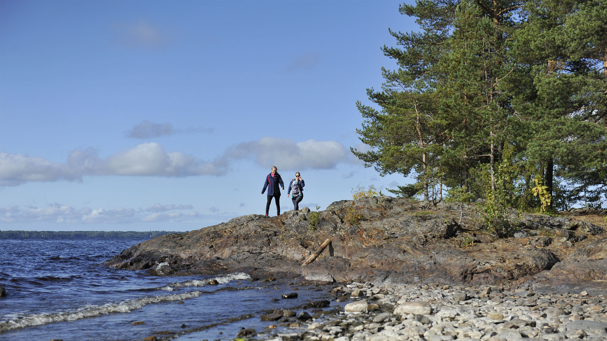 Kaksi henkilö ulkoilemassa järven rannalla.