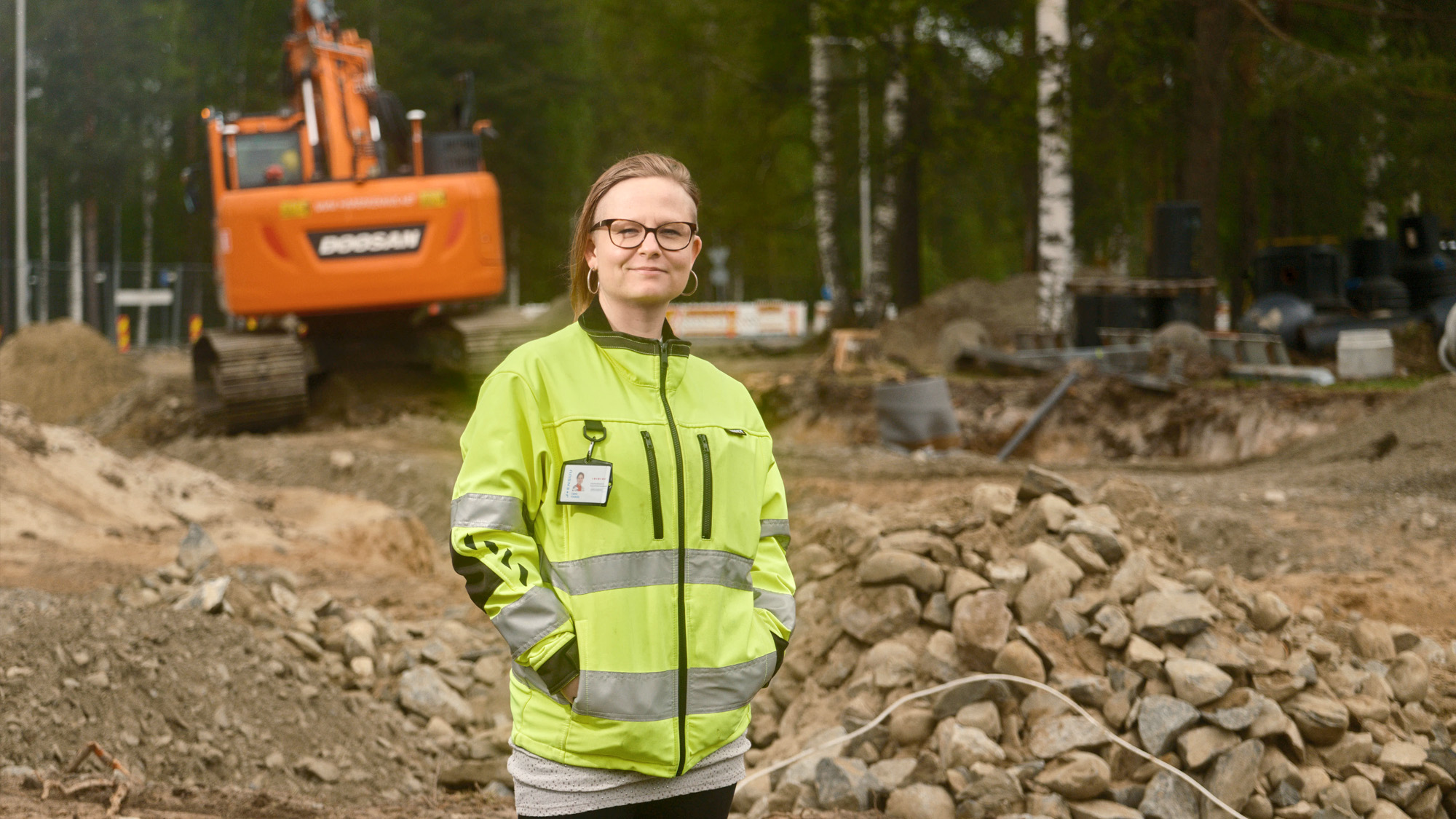 Keltaiseen huomiotakkiin pukeutunut henkilö. Taustalla rakennustyömaa ja maansiirtokone.