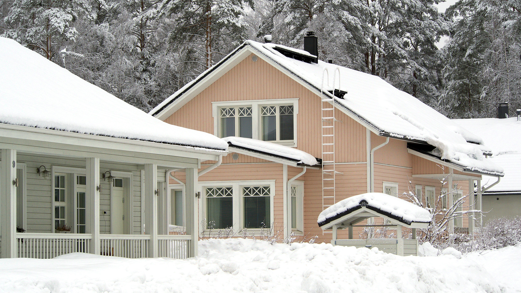 Omakotitaloja talvella, lunta on kerääntynyt talojen katoille ja pihamaille.