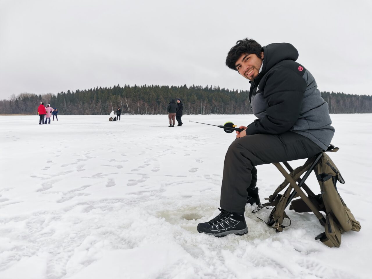 mies istuu pilkillä järven jäällä
